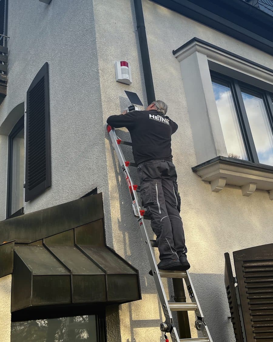 Monteur von Heine Sicherheitstechnik montiert auf einer Leiter eine Außensirene an der Hausfassade