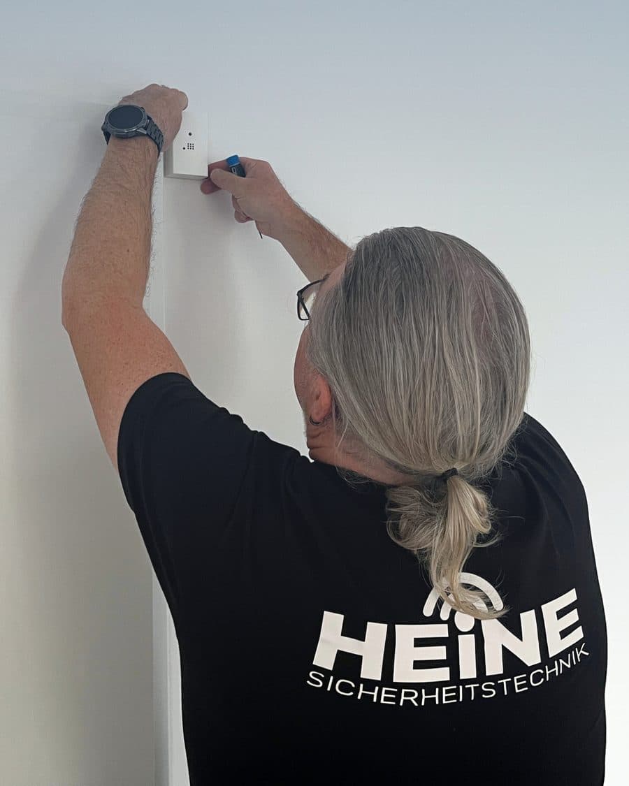 Monteur setzt einen Funkmelder oben an eine weiße Wand