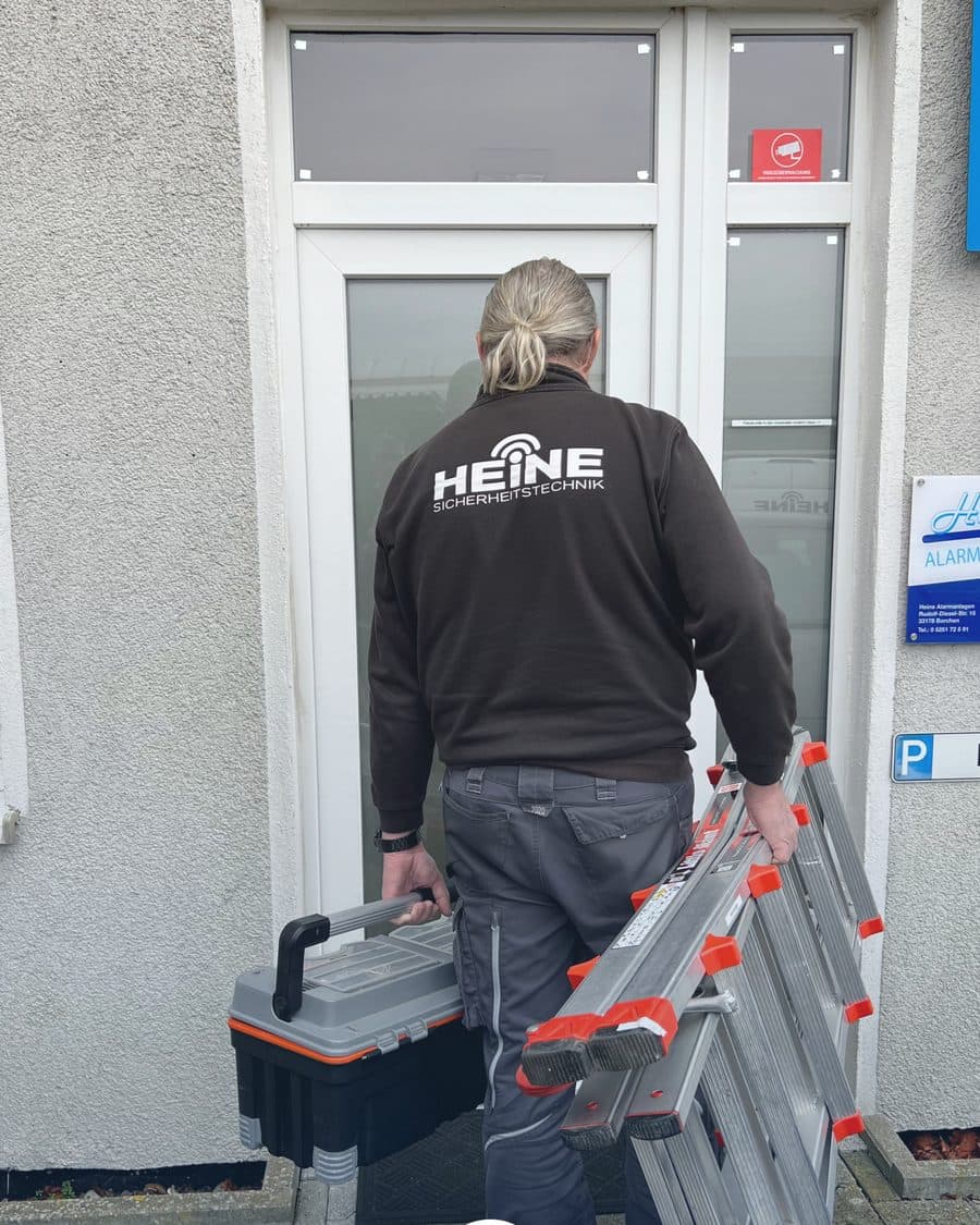 Monteur mit Leiter und Werkzeugkoffer vor dem Firmeneingang von Heine Sicherheitstechnik in Borchen