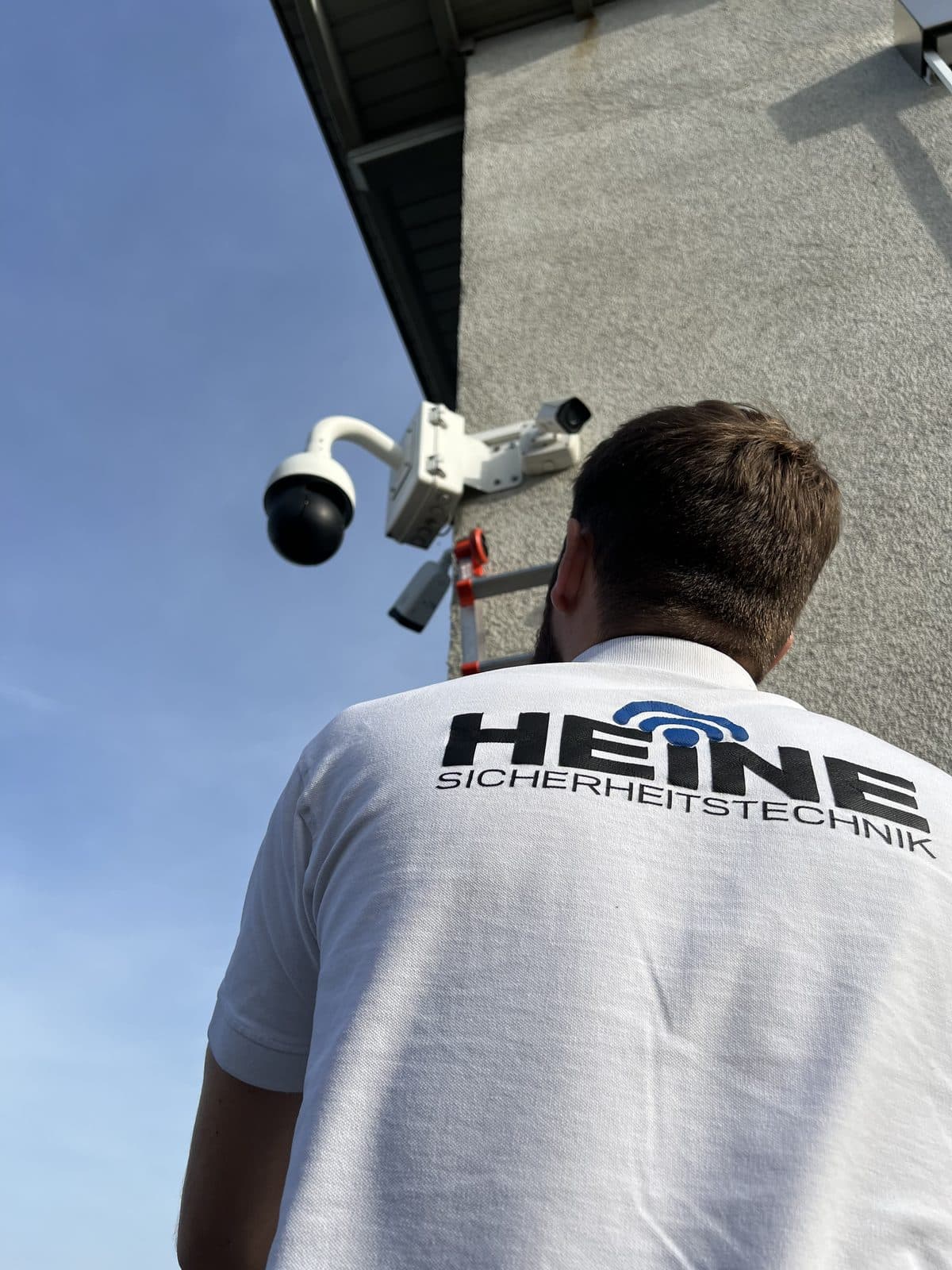 Heine-Techniker vor zwei frisch montierten Überwachungskameras an einer Hausfassade